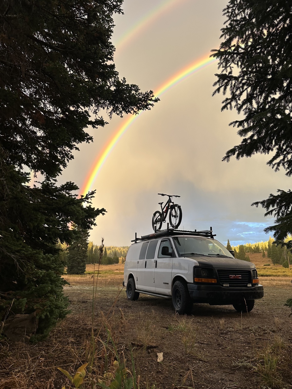 The completed van build parked in the mountains with a double rainbow